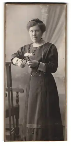 Fotografie unbekannter Fotograf und Ort, Portrait einer elegant gekleideten Frau mit Blume in der Hand