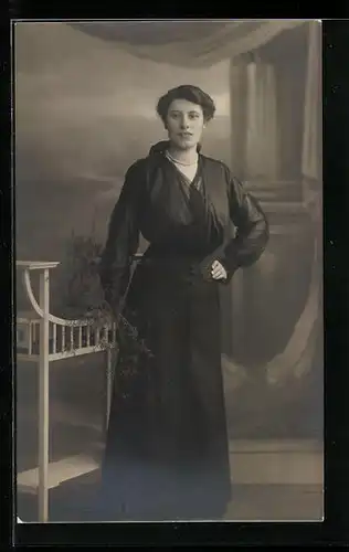 Foto-AK Junge Frau im schwarzen Kleid in einer Studiokulisse