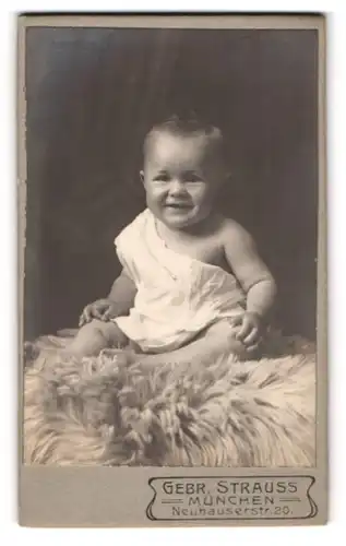 Fotografie Gebr. Strauss, München, Neuhauserstr. 20, Portrait süsses Baby im Hemdchen auf einem Fell sitzend