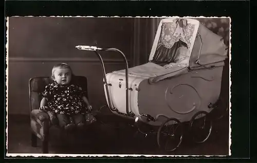 Foto-AK Süsses kleines Mädchen auf einem Kindersesselchen, daneben ihr Kinderwagen