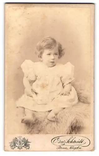 Fotografie Osw. Schmidt, Pirna, Ecke Grohmann- & Jackobäerstr., Kind im Kleid sitzt auf einem Fell