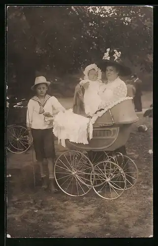 Foto-AK Mutter mit Kind und Knabe hinter einem Kinderwagen im Grünen
