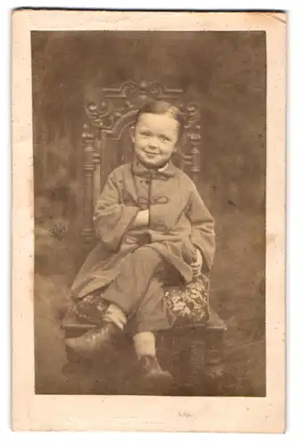 Fotografie unbekannter Fotograf und Ort, junger Knabe posiert sitztend mit überschalgenen Beinen im Atelier