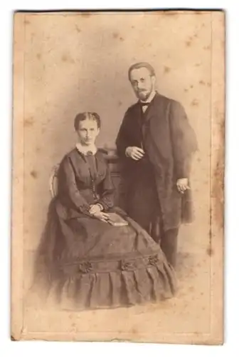 Fotografie Maler Buchner, Stuttgart, junges Paar im dunklen Kleid und Anzug mit Brosche und Fliege, 1870