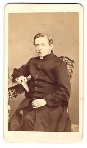 Fotografie Franz Neumayer, München, Neue Pferdstr. 2, junger Pastor im Talar mit Collar sitzend im Atelier