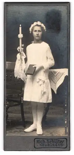 Fotografie Rich. Schlüter, Neuburg a. D., junges Mädchen zu ihrer Kommunion im weissen Kleid mit Kerze und Haarschmuck