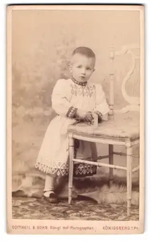 Fotografie Gottheil & Sohn, Königsberg, G. Münz-Strasse 6, Kleinkind mit kurzen Haaren im bestickten Kleidchen