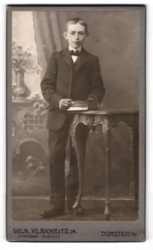 Fotografie Wilh. Klanneitz Jr., Dorsten i. W., Knabe im schwarzen Anzug mit Fliege und Buch in der Hand