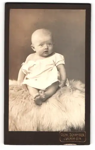 Fotografie Alfred Schreiber, Jarmen, süsses kleines Kind im weissen Kleid auf Fell sitzend