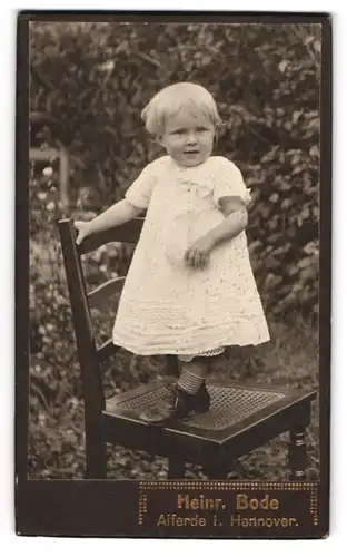 Fotografie Heinr. Bode, Alferde i. Hannover, süsses Kind im weissen Kleid auf Stuhl stehend