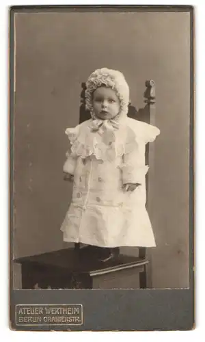 Fotografie Atelier Wertheim, Berlin, Oranienstr., süsses kleines Kind im weissen Mantel auf Stuhl stehend