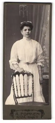 Fotografie A. Popken, Altona, Königstr. 97, hübsche junge Dame im weissen Kleid hinter einem Stuhl stehend