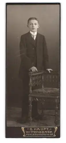 Fotografie Georg Haupt, Wittenberge, Perlebergerstrasse 150, stattlicher Knabe im schwarzen Anzug an einer Bank