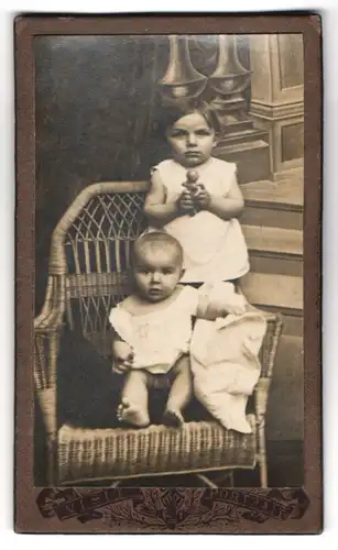 Fotografie unbekannter Fotograf und Ort, zwei kleine Kinder im weissen Kleid mit Spielzeug