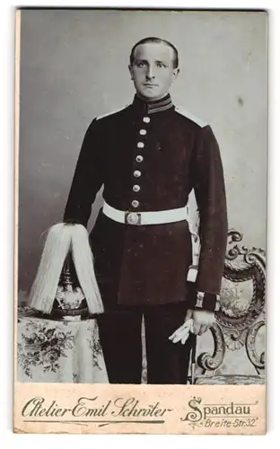 Fotografie Emil Schröter, Spandau, Soldat in Gardeuniform mit Pickelhaube Rosshaarbusch auf dem Tisch