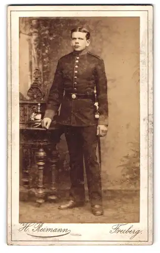 Fotografie H. Reimann, Freiberg i. Sa., junger sächsischer Artillerist un Uniform mit Pickelhaube auf dem Tisch