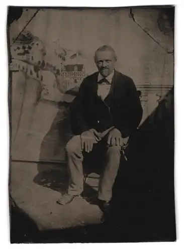 Fotografie Ferrotypie älterer Herr im Anzug sitzend vor Studiokulisse