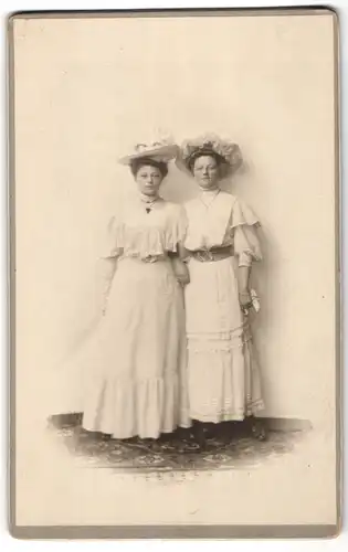Fotografie unbekannter Fotograf und Ort, zwei hübsche junge Damen in weissen Kleidern mit Hüten posiern im Atelier, 1908