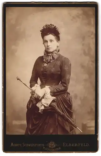 Fotografie Moritz Schweisfurth, Elberfeld, junge Frau im dunklen floral bestickten Kleid mit Schirm und Kopfbedeckung
