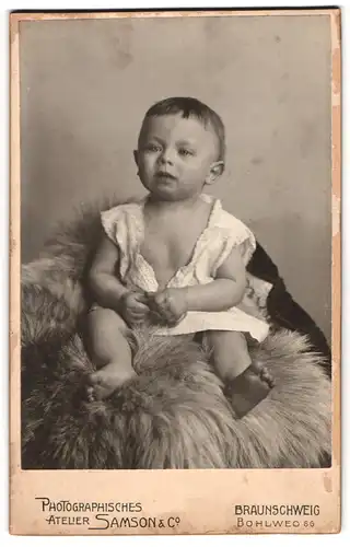 Fotografie Atelier Samson & Co, Braunschweig, Bohlweg 66, süsses Kind im weissen Kleid auf Fell sitzend
