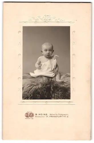 Fotografie B. Heinz, Frankfurt a. M., Brückenstr. 54, niedliches Kind im weissen Kleid auf Fell sitzend