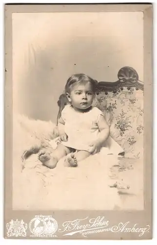 Fotografie F. Frey Söhne, Amberg, niedliches Kind im weissen Kleid auf Fell sitzend
