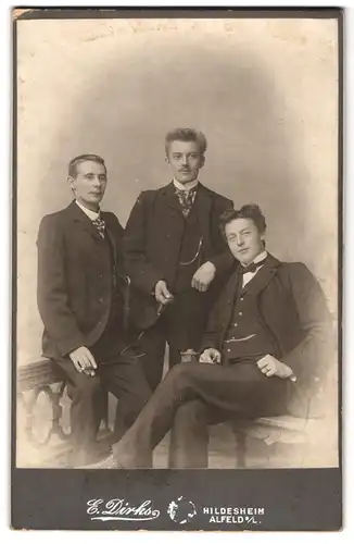 Fotografie E. Dirks, Hildesheim, Alfeld a. L., drei elegante Männer im schwarzen Anzug mit Zigarre