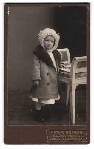 Fotografie Peter Ederer, Landshut i. B., Seligentalerstr. 18, Portrait süsses Kleinkind mit Mütze im Mantel