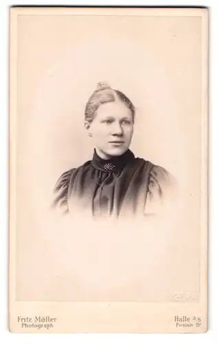 Fotografie Fritz Möller, Halle a. S., Poststr. 19, Portrait blonde junge Frau mit Dutt und Brosche am Kleiderkragen