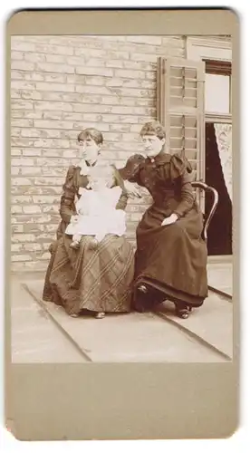 Fotografie Fotograf unbekannt, München, zwei elegant gekleidete Frauen mit kleinem Mädchen auf dem Schoss