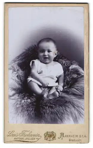 Fotografie Louis Frohwein, Mannheim, Breitestr., niedliches Baby im weissen Hemdchen auf einem Fell sitzend