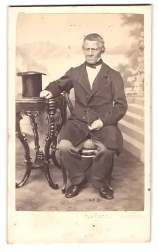 Fotografie L. Rüsch, Rheineck, älterer Herr im Anzug mit Zylinder auf dem Tisch