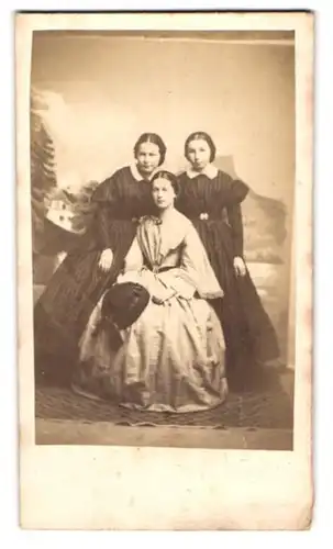 Fotografie L. Rüsch, Rheineck, drei junge Damen in dunklen karierten und im hellen Kleid posieren im Atelier