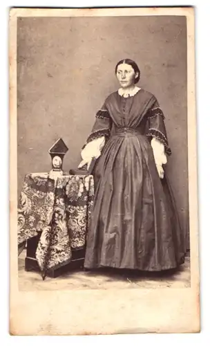 Fotografie Louis Roulet, Bienne, junge Frau im dunklen Kleid posiert stehend an einem Tisch