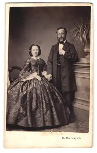 Fotografie E. Heironymi, Zürich, älterer Mann mit junger Frau im Reifrockleid halten Händchen