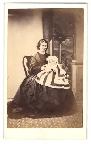 Fotografie unbekannter Fotograf und Ort, junge Mutter im schwarzen Kleid mit ihrem Baby auf dem Schoss