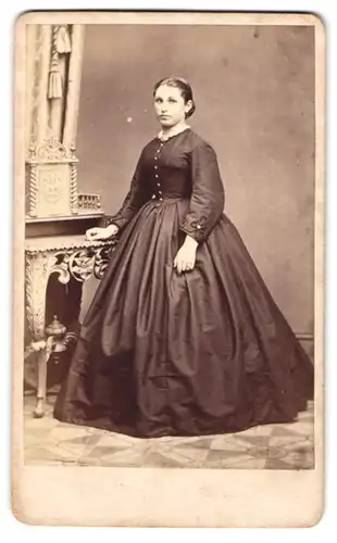 Fotografie Franz Boden, Glatz, junge Frau im Reifrockkleid stehend am Sekretär