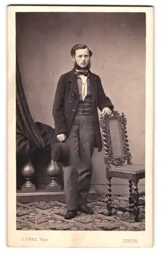 Fotografie J. Ganz, Zürich, junger Mann im Anzug mit Backenbart und Hut in der Hand