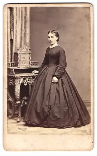 Fotografie Franz Boden, Glatz, junge Frau im schwarzen Kleid stehend am Sekretär