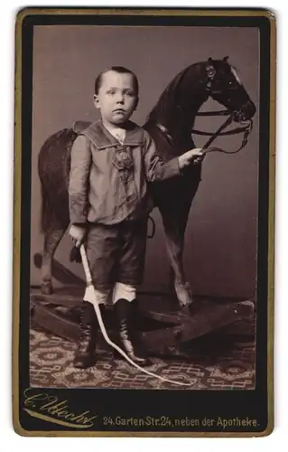 Fotografie Carl Utrecht, Berlin, Knabe mit seinem Schaukelpferd und Peitsche im Atelier