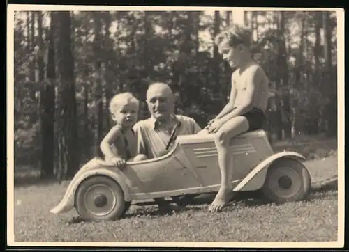 Fotografie blonder Knabe im Tretauto, Seifenkiste, Spielzeug-Auto sitzend