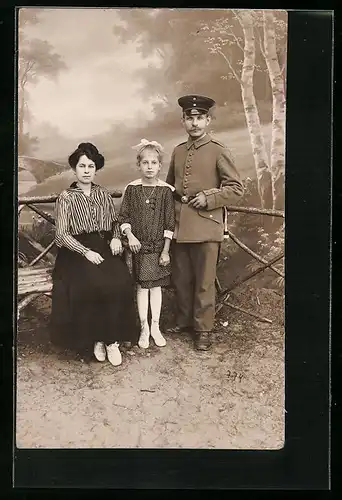 Foto-AK Familie, Vater in Uniform posiert vor Studiokulisse