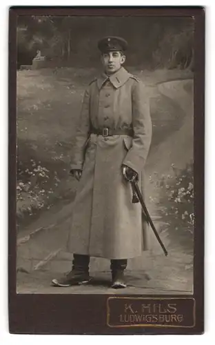 Fotografie K. Hils, Ludwigsburg, Soldat in Uniform Mantel Regimetn 65 mit Säbel, Spornschuhe