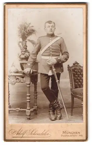 Fotografie Adolf Schindeler, München, bayrischer Soldat in Uniform mit Säbel und Pickelhaube auf dem Tisch