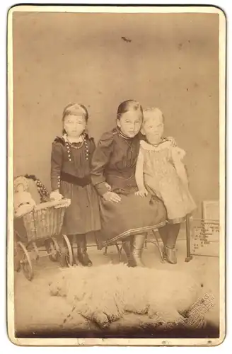 Fotografie unbekannter Fotograf und Ort, drei junge Mädchen mit ihrem Puppenwagen und Puppe im Atelier