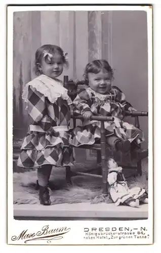 Fotografie Max Baum, Dresden, zwei niedliche Mädchen im karierten Kleidern mit Puppe zu den Füssen