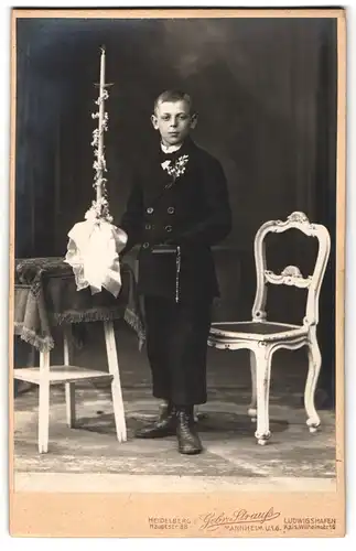 Fotografie Gebr. Strauss, Ludwigshafen, junger Knabe im Anzug zu seiner Konfirmation mit langer Kerze in der Hand