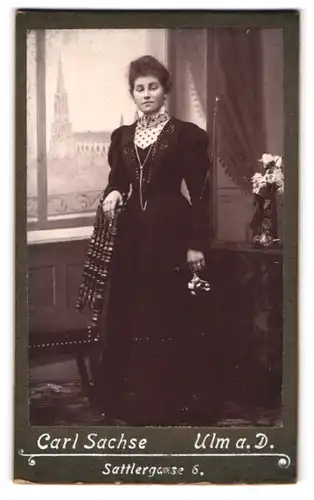 Fotografie Carl Sachse, Ulm a. D., junge Frau im dunklen Kleid vor einer Studiokulisse