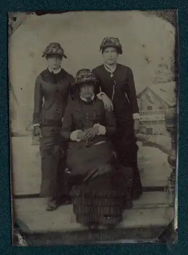 Fotografie Ferrotypie drei Damen in dunklen Kleidern mit Hüten vor einer Studiokulisse