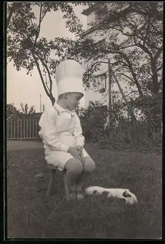 Fotografie Knabe mit Kochmütze nebst Katze die im Gras liegt